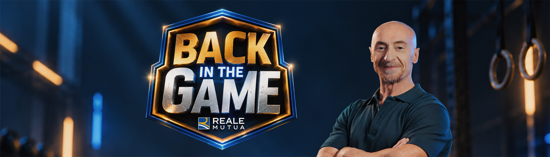 Primo piano di Jury Chechi sorridente con a fianco il logo del format 'Back in the game' e il logo di Reale Mutua, sullo sfondo una palestra e l'attrezzo con i cerchi, specialità sportiva del grande campione