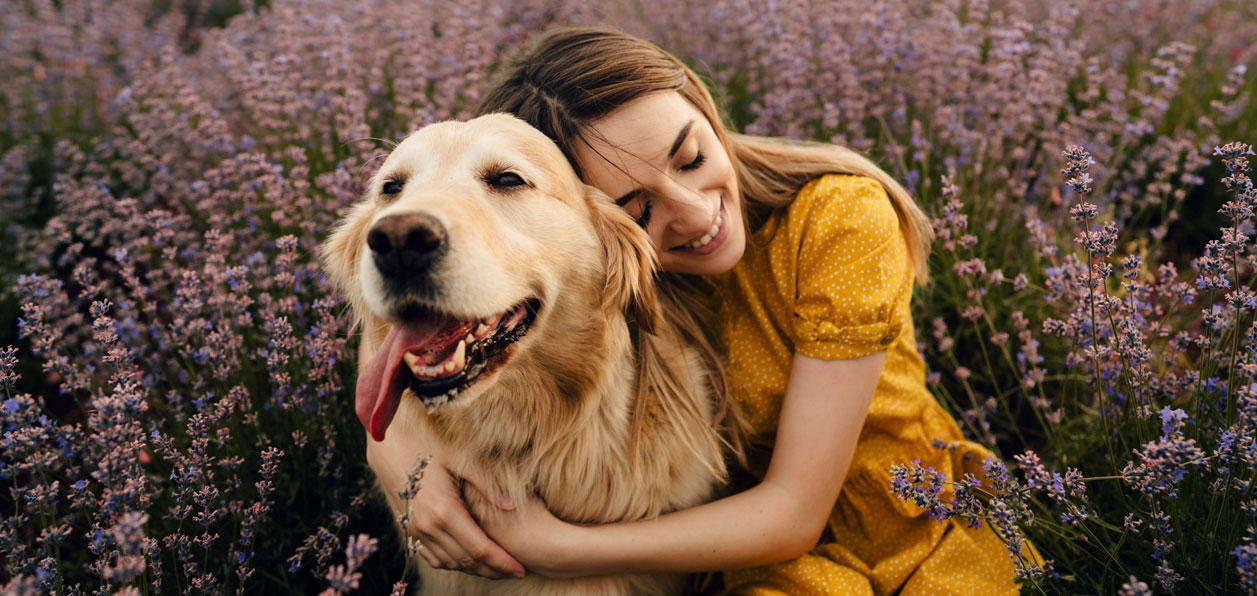 Ragazza che abbraccia il suo cane mentre giocano in un campo di fiori